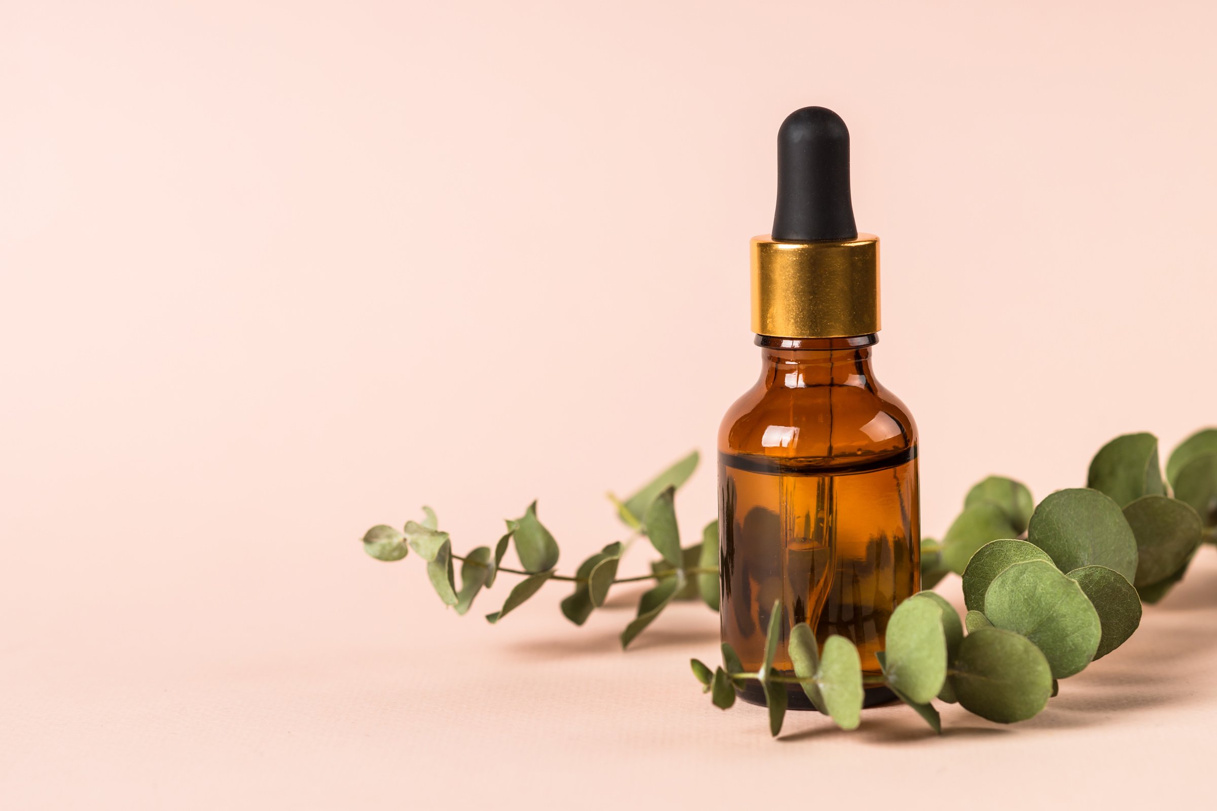 Serum Bottle with Fresh Leaves at Pastel Background.